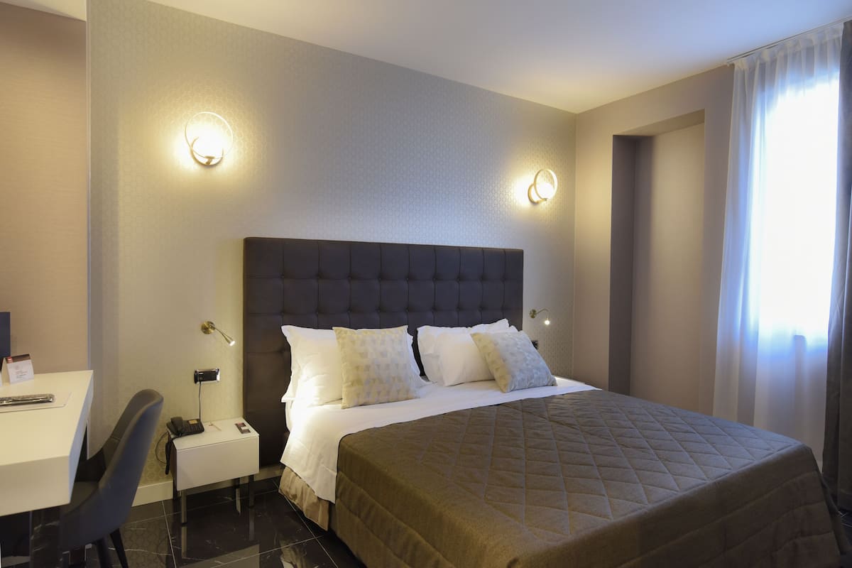 A hotel room with a large bed, a desk, and two wall-mounted lamps.
