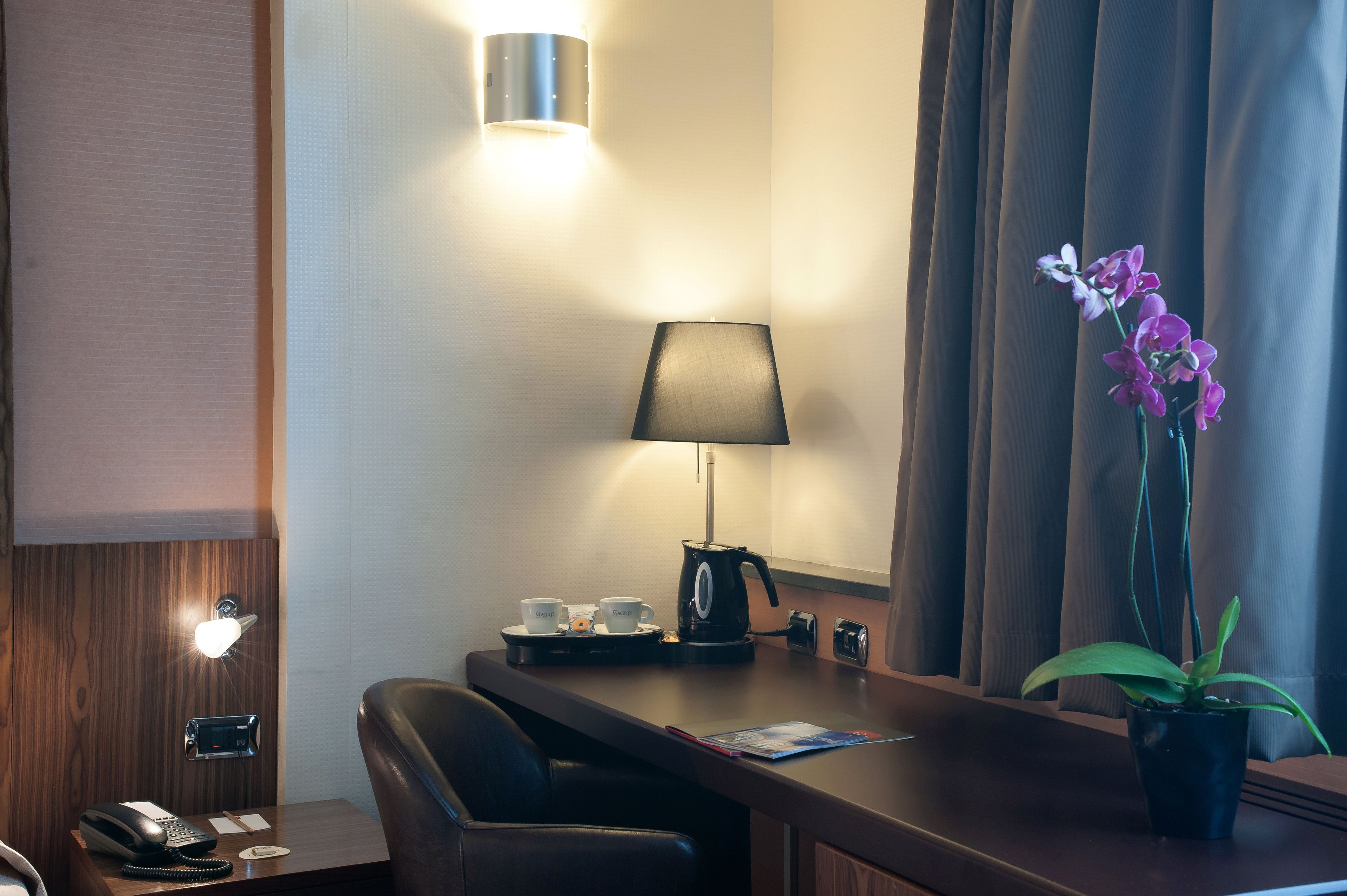 Une chambre d’hôtel équipée d’un bureau, d’une lampe, d’un téléphone, d’une machine à café, de tasses et d’une orchidée en pot.