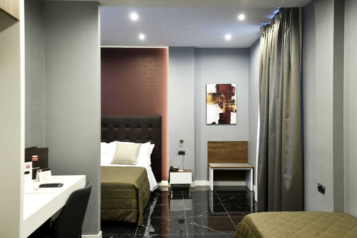 A modern hotel room with a bed, a desk, a bench, and a small table.