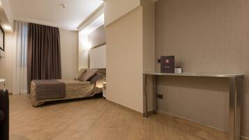 Habitación de hotel con cama, mesita de noche, lámpara y estante en la pared.