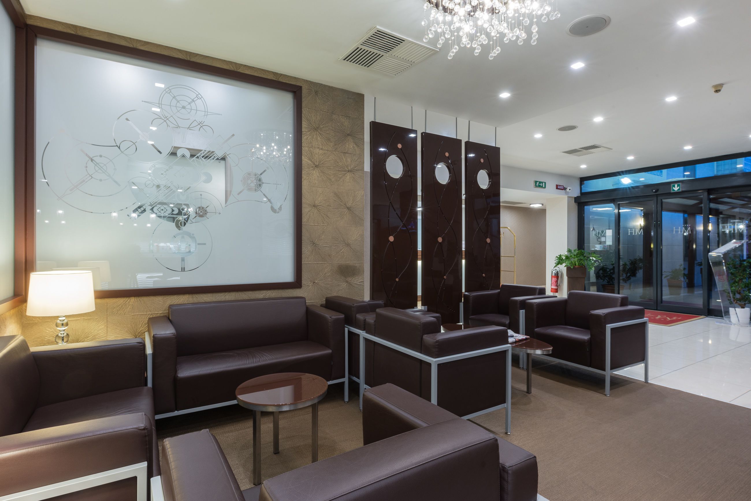 Um hall de hotel moderno com assentos de couro, uma grande obra de arte abstrata e um candelabro.