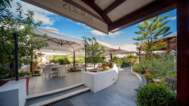 An outdoor patio area with tables and chairs, surrounded by potted plants and umbrellas. - Magris Hotel (Naples)