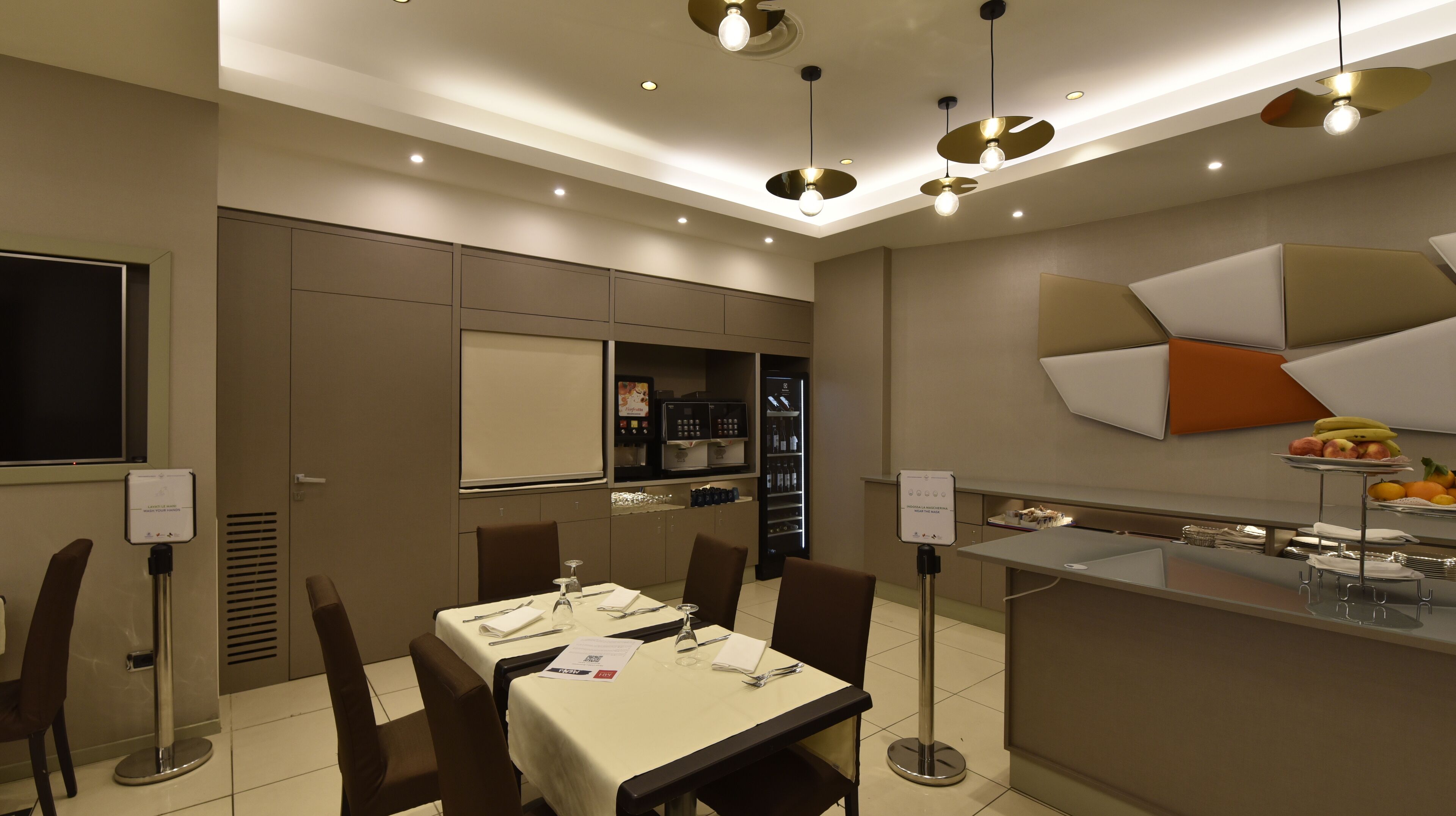 A modern dining area with a buffet setup, including a refrigerator stocked with beverages and a fruit display.