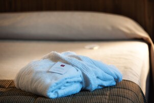 Un asciugamano bianco, piegato con cura, su una poltrona in tessuto marrone con un'etichetta, posizionato su un letto con un cuscino bianco.