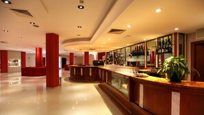 Een ruime lobby met een gebogen receptiebalie, een bar met flessenkasten en een grote potplant.