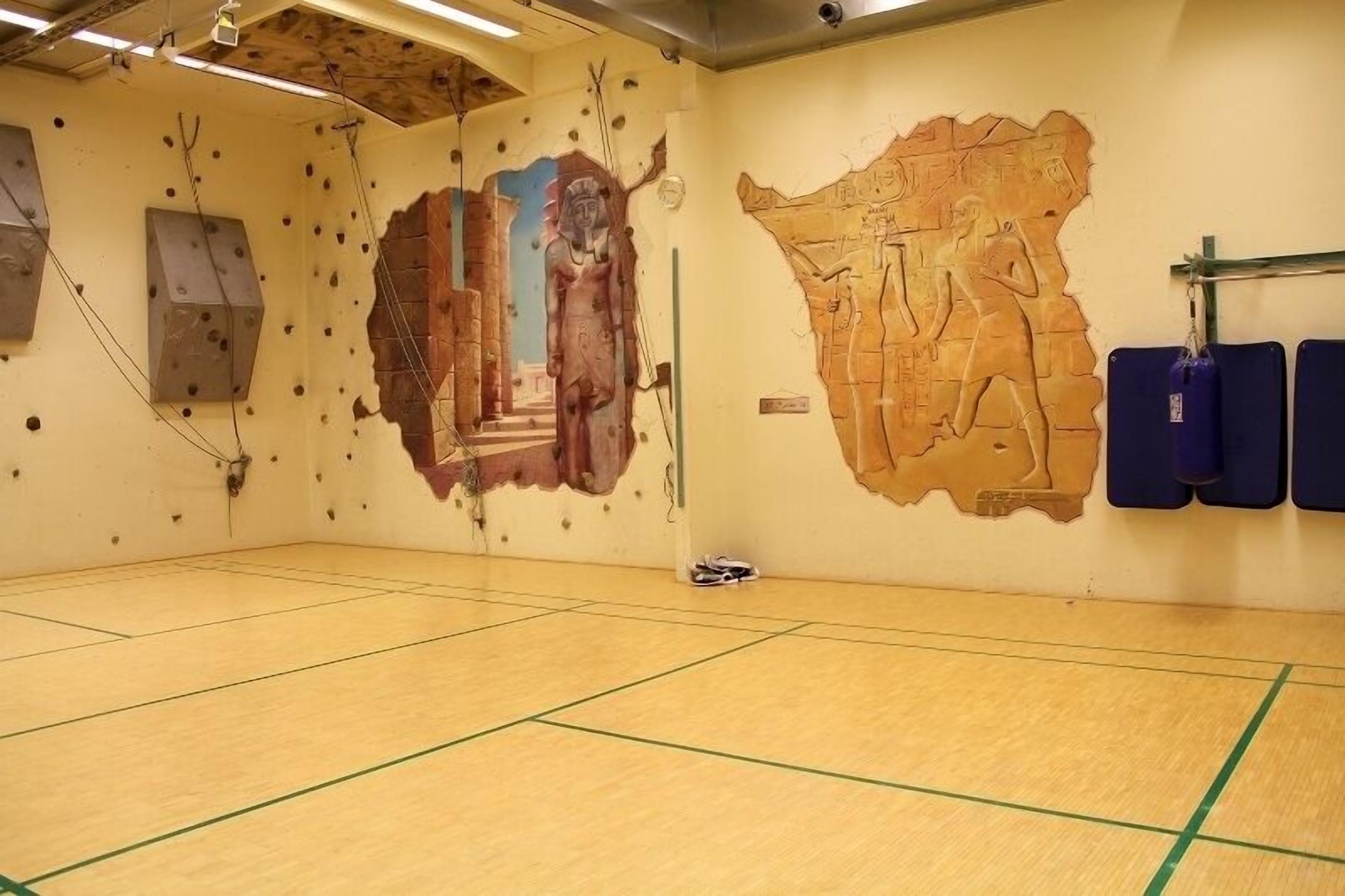 A gym with wooden flooring, climbing walls, and Egyptian-themed murals.