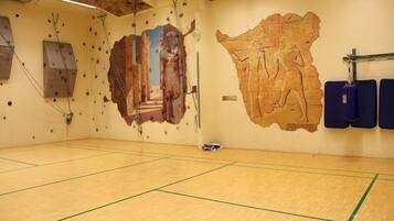 A gym with wooden flooring, climbing walls, and Egyptian-themed murals.