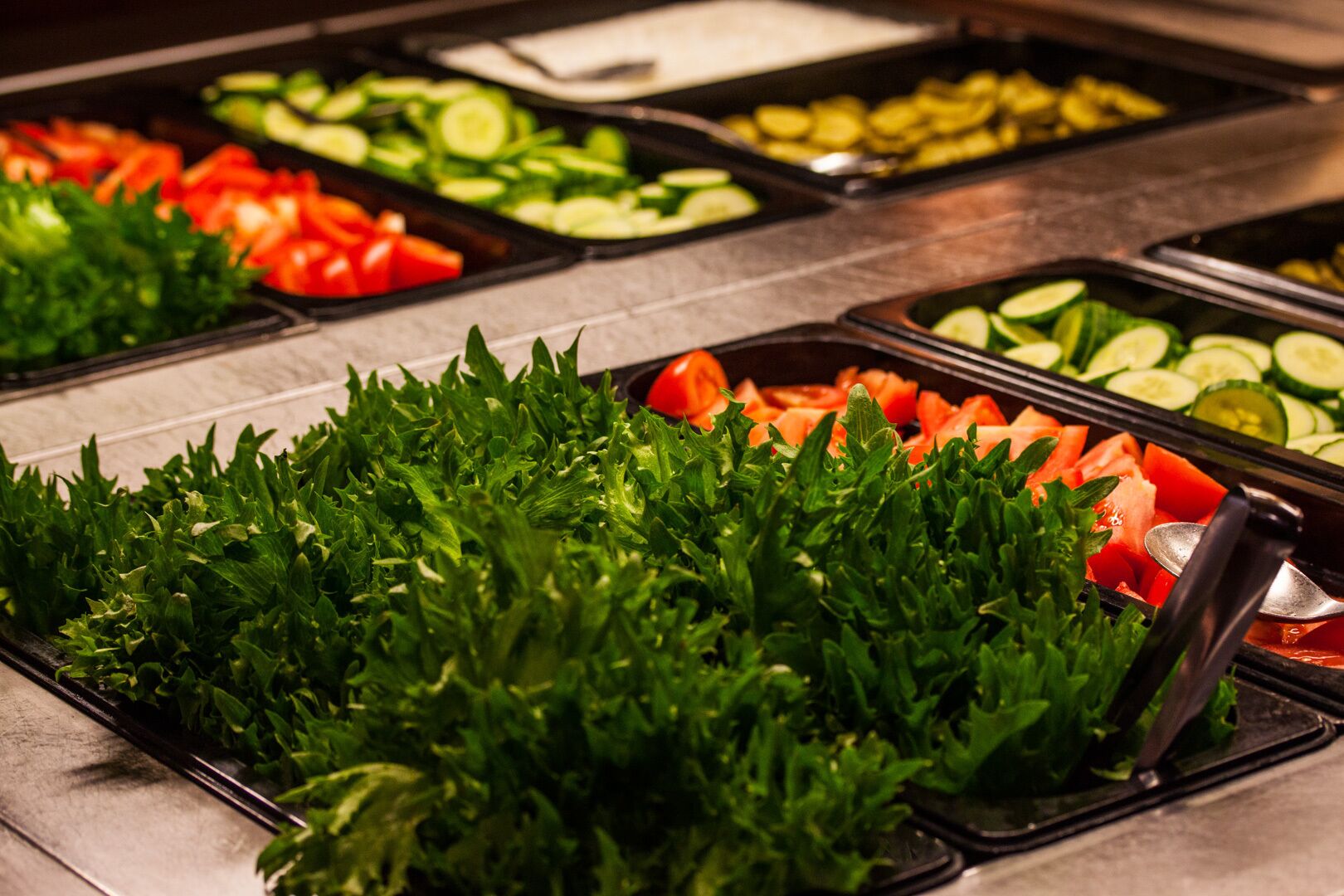 A buffet with various fresh vegetables including lettuce, tomatoes, cucumbers, and carrots.