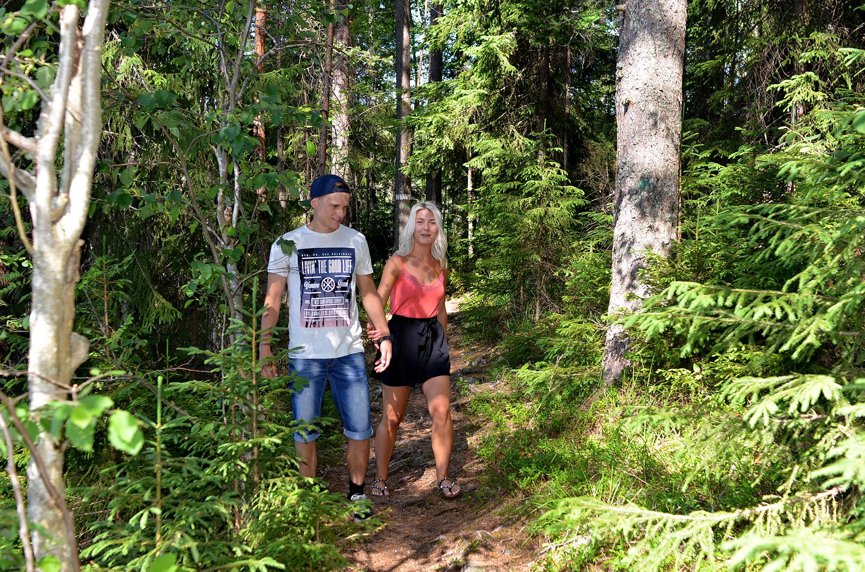 Deux personnes se promènent sur un sentier forestier, entourées d’une végétation luxuriante.