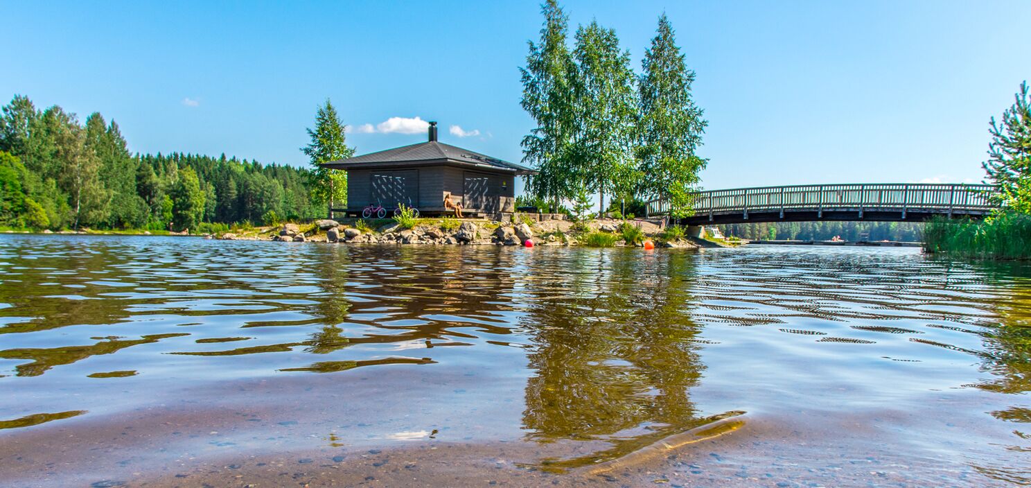 Una cabaña junto al lago con muelle, rodeada de árboles y un puente.