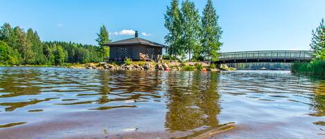 Una cabaña junto al lago con muelle, rodeada de árboles y un puente.