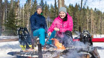 Two people sitting by a campfire in a snowy forest.