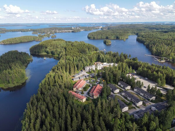 An aerial view of a resort with multiple buildings, a parking area, and a lake surrounded by dense forests.
