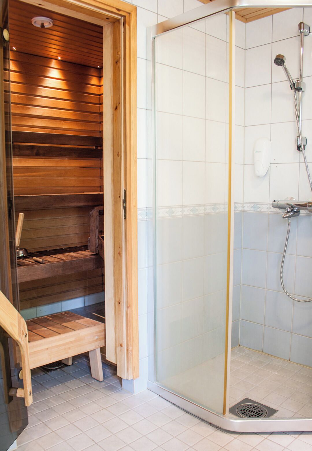 A shower with a glass door, a wooden bench, and a tiled floor.