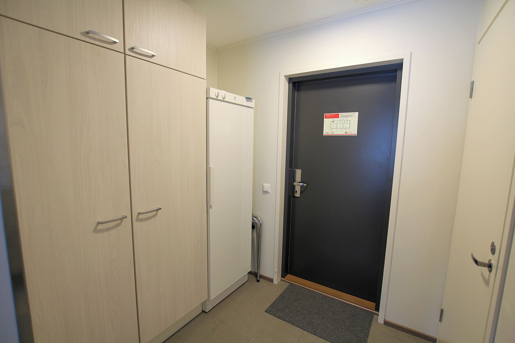 A hallway with a door, a trash bin, and a small mat at the entrance.