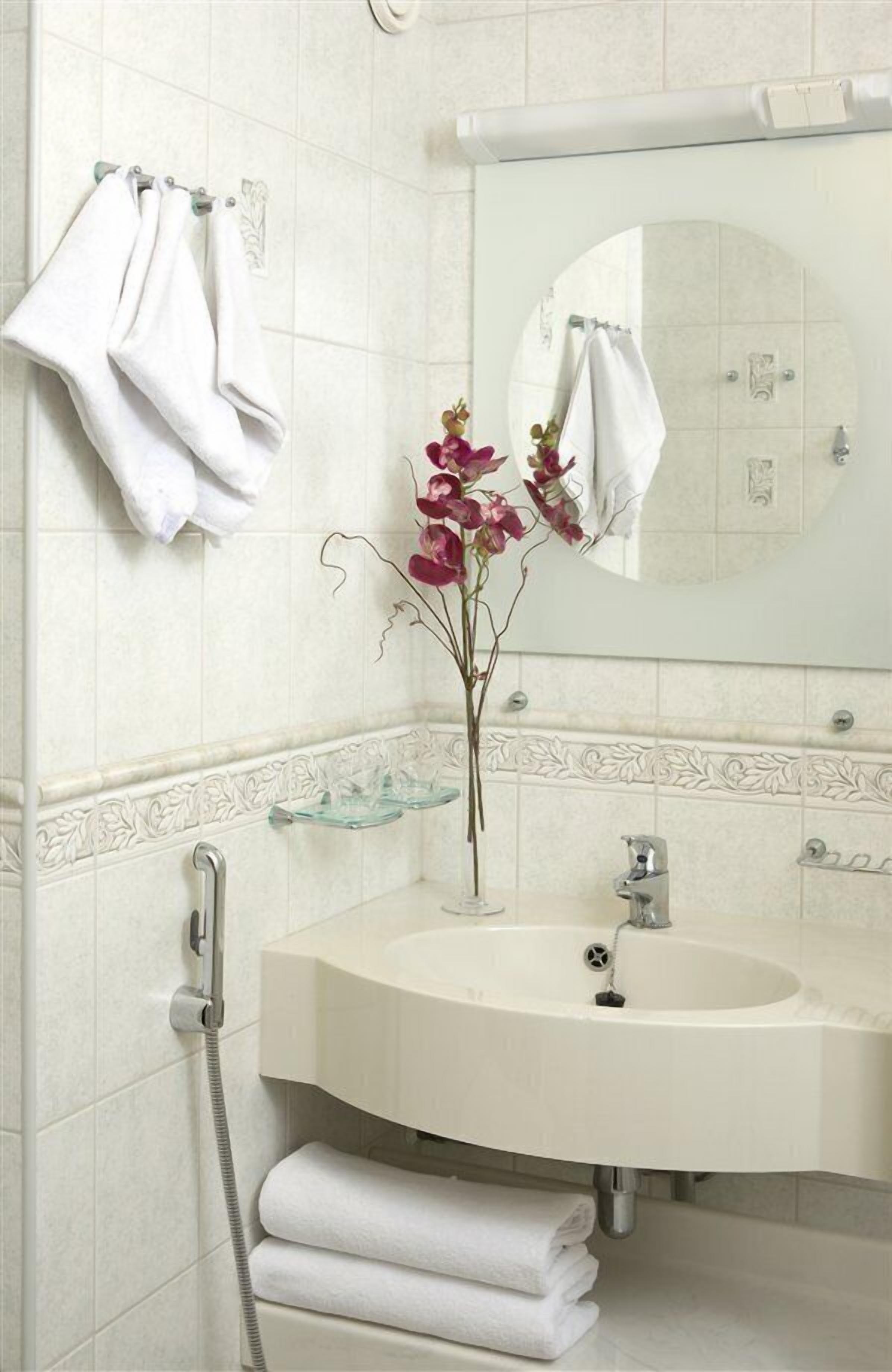 A bathroom with a white sink, a mirror, and two towels hanging on hooks.