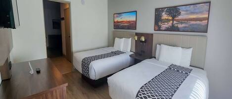 A hotel room with two beds, a wooden desk, and artwork on the walls.