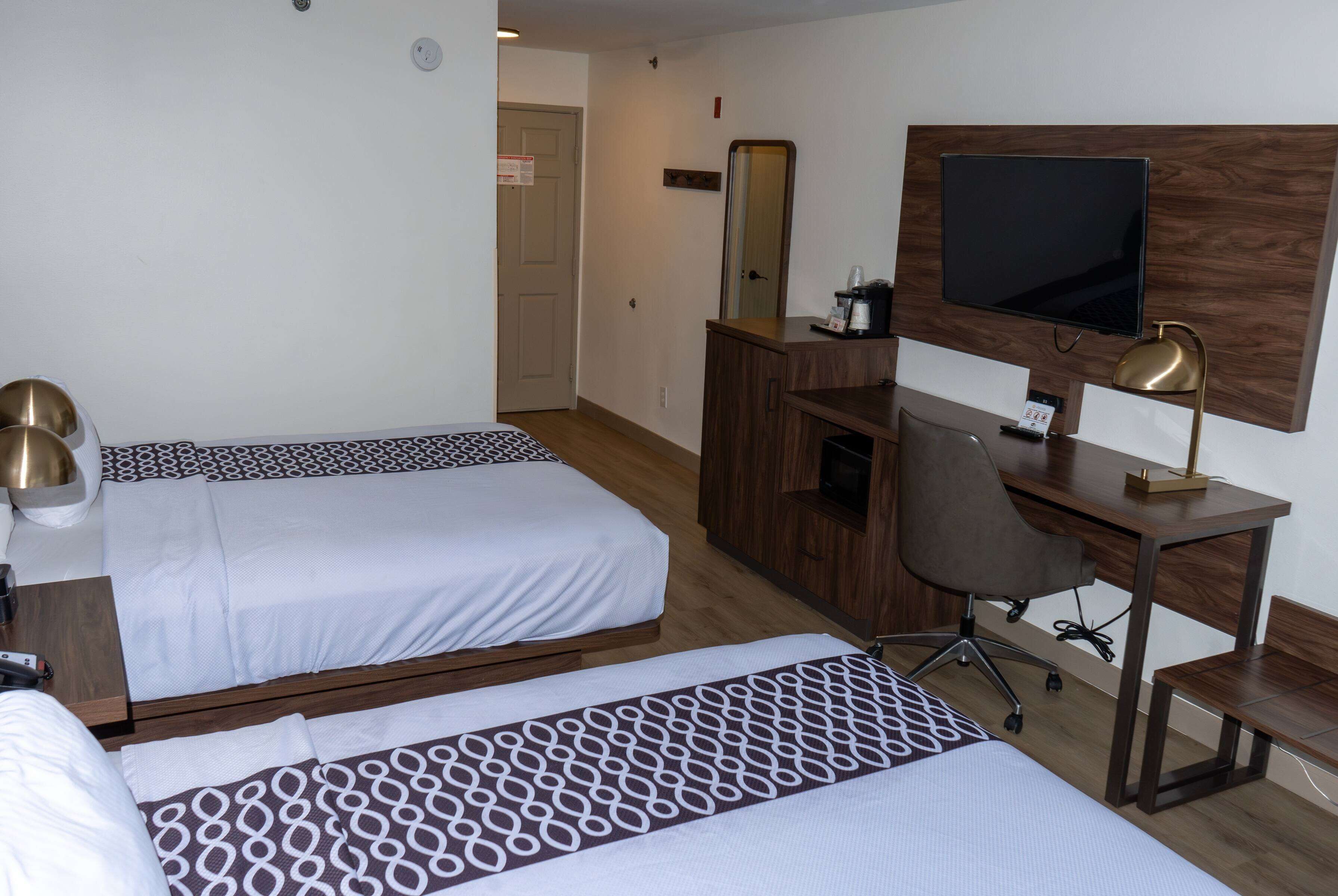 A hotel room with two beds, a desk with a computer, a TV, and a mirror.