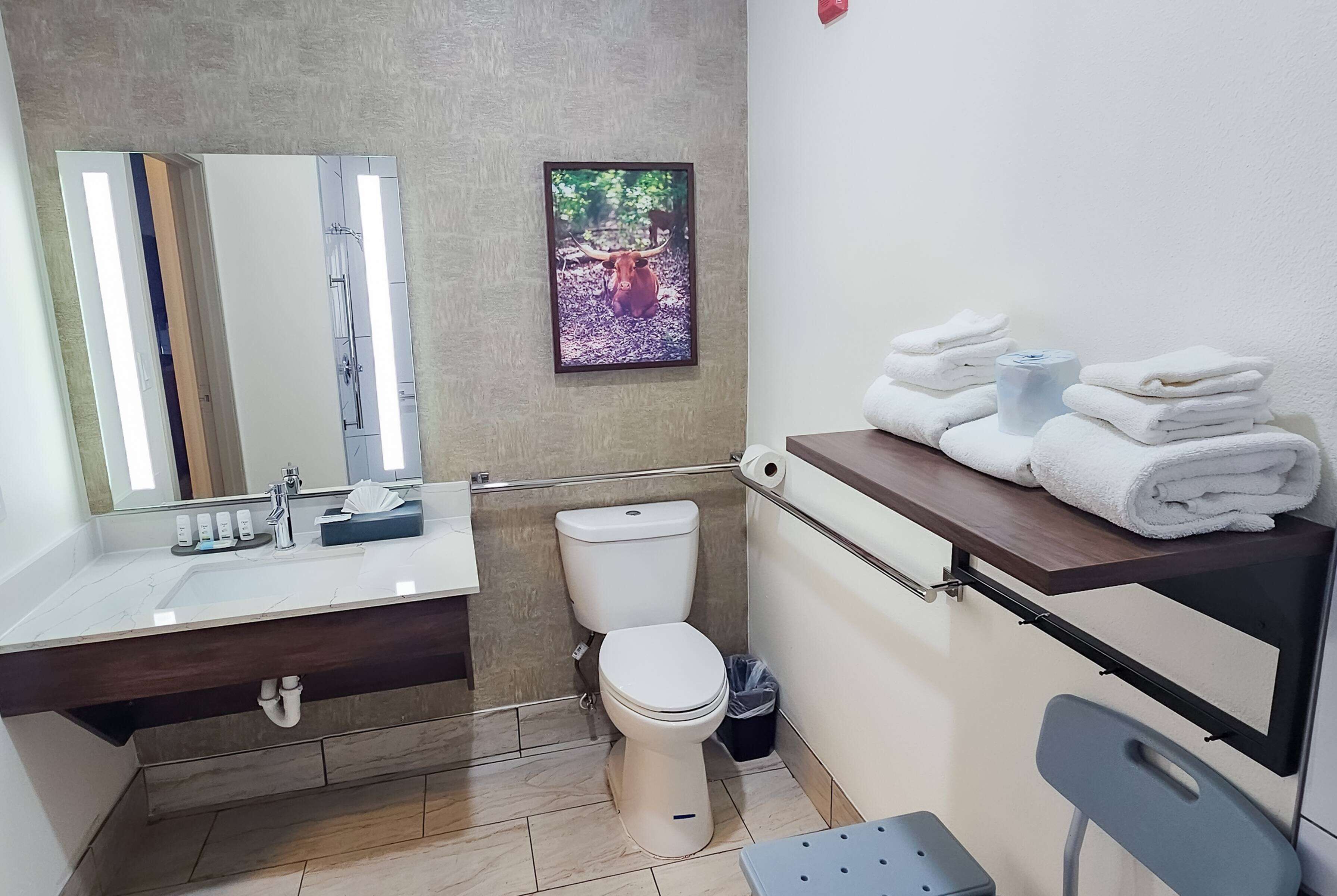A bathroom with a white sink, mirror, toilet, and a towel rack with folded towels.