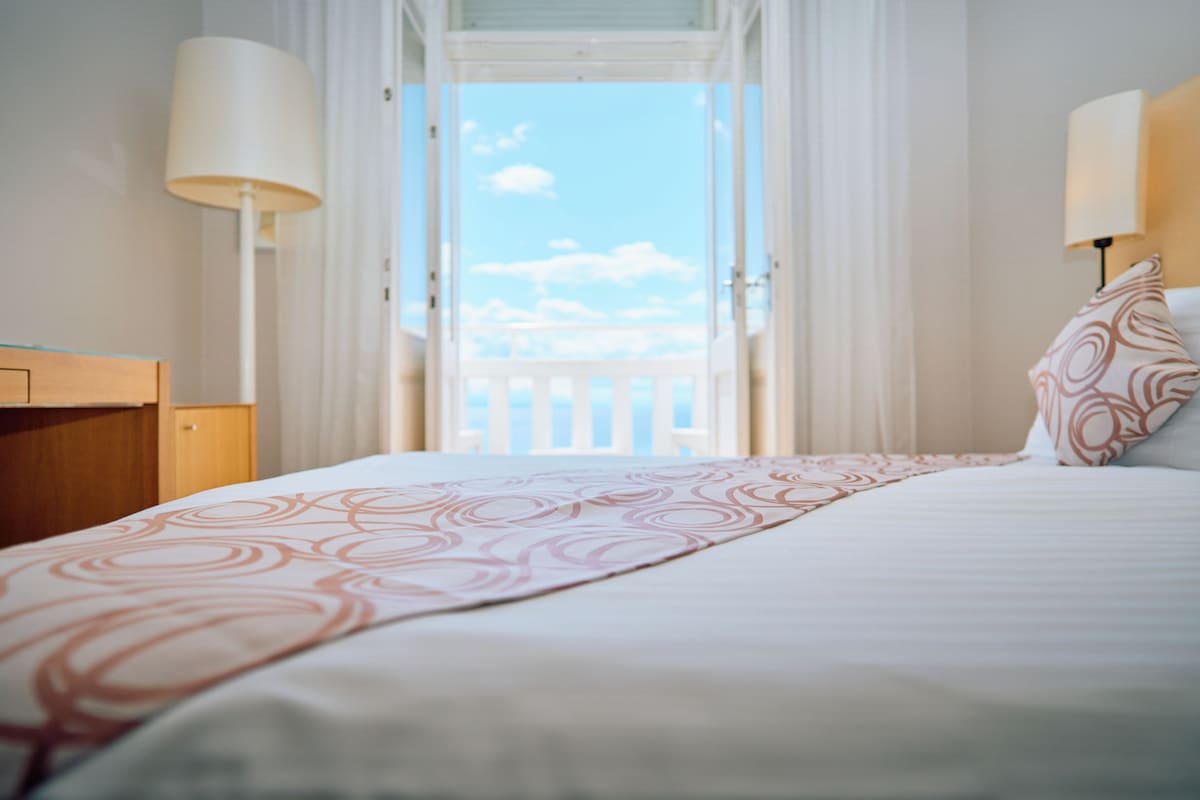 Une chambre d’hôtel avec un lit, une table de chevet, une lampe et une vue sur un balcon.