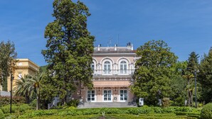 A large, historic building with a symmetrical facade, surrounded by well-manicured gardens and tall trees. - Astoria Hotel Opatija**** (Opatija)