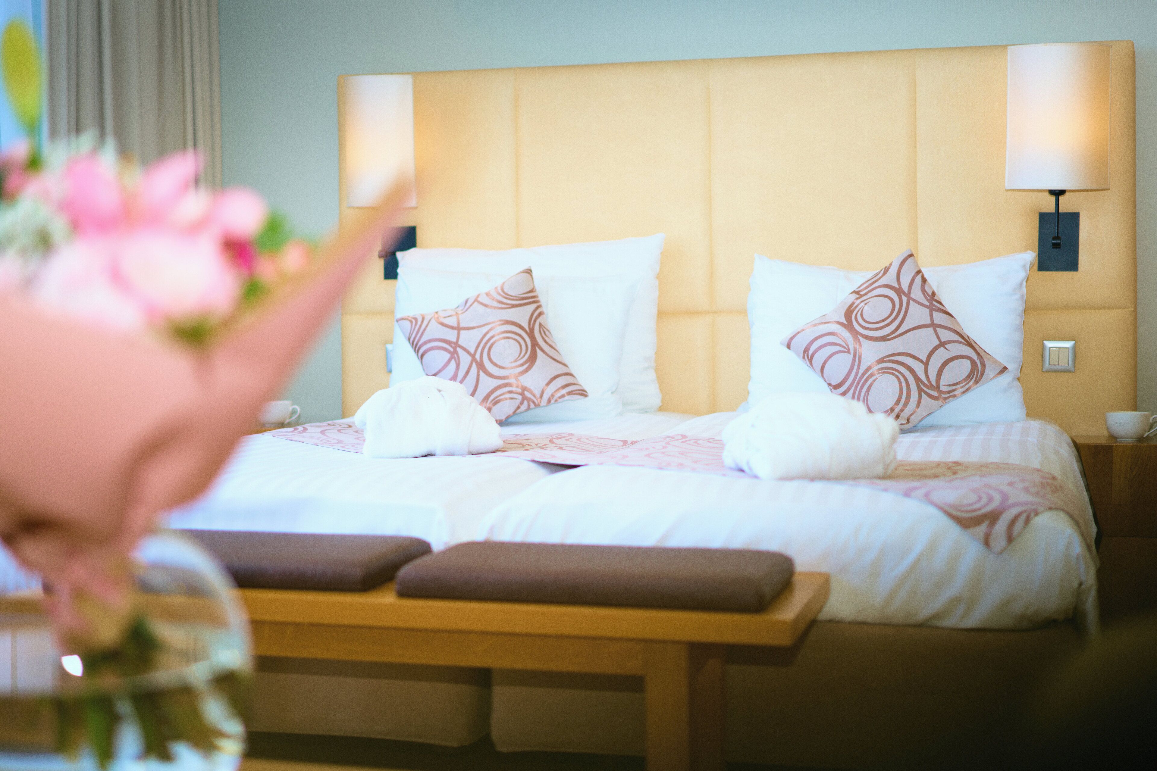 Ein Hotelzimmer mit einem großen Bett, zwei Nachttischlampen, einer hölzernen Bank und einem Blumenstrauß.