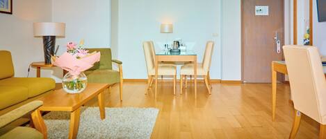 A living room with a sofa, a coffee table with a vase, a dining table with chairs, and a wooden floor.
