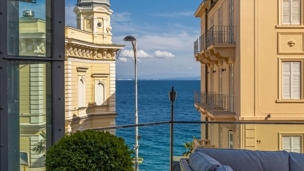 A balcony with a view of the sea, a historic building, and a modern glass structure. - Astoria Hotel Opatija**** (Opatija)