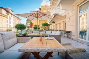 Un patio al aire libre con mobiliario de mimbre, una mesa de madera y un paraguas grande.