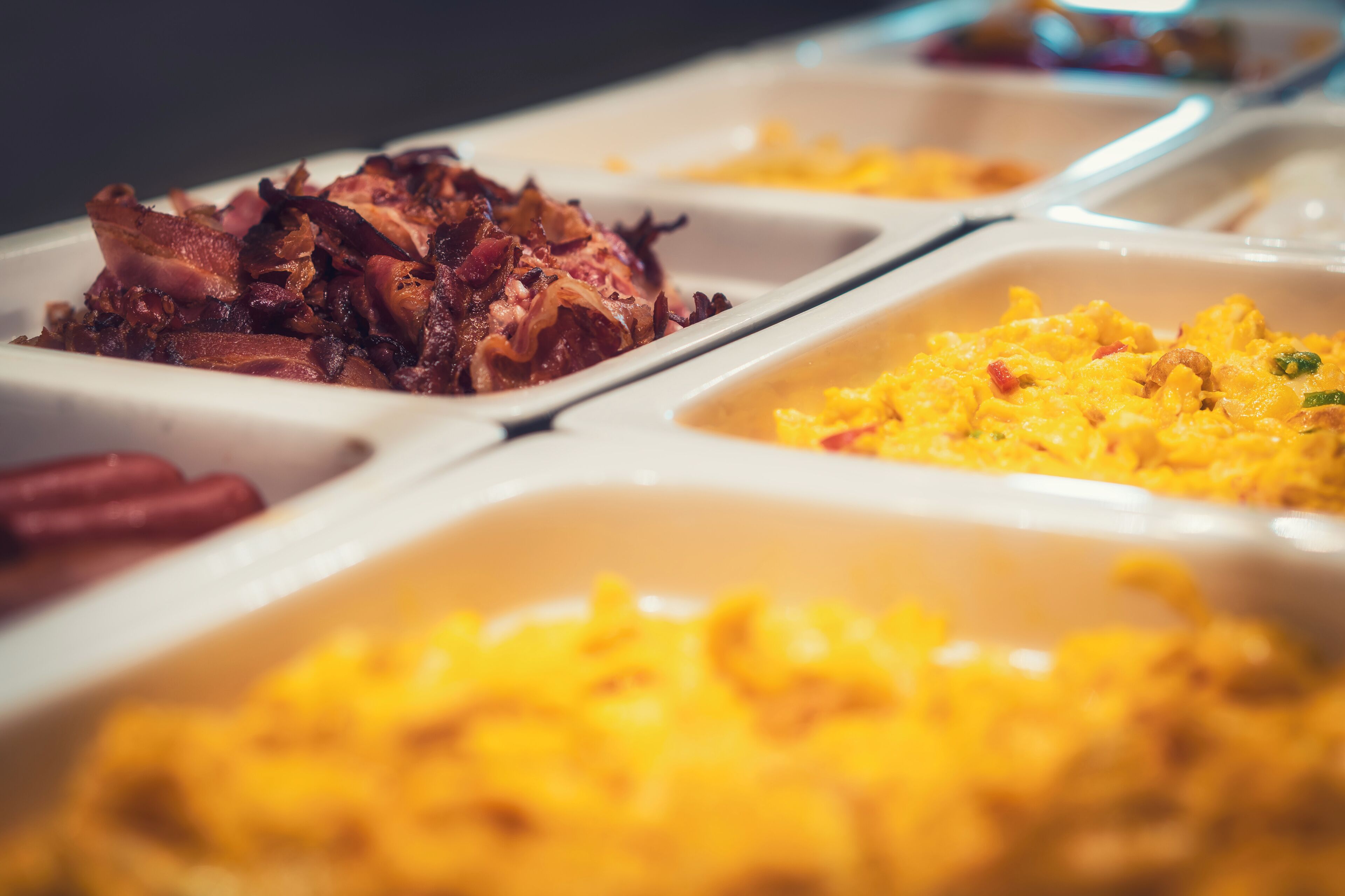 A buffet with various dishes including scrambled eggs, bacon, and rice.