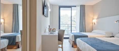 Hotellihuone, jossa on kaksi sänkyä, työpöytä, tuoli, televisio ja ikkuna, jossa on verhot.