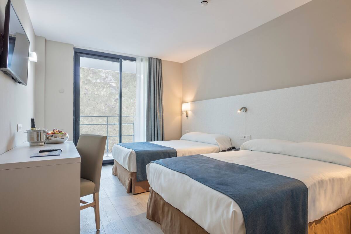 Een hotelkamer met twee bedden, een bureau, een stoel, een televisie en een raam met gordijnen.