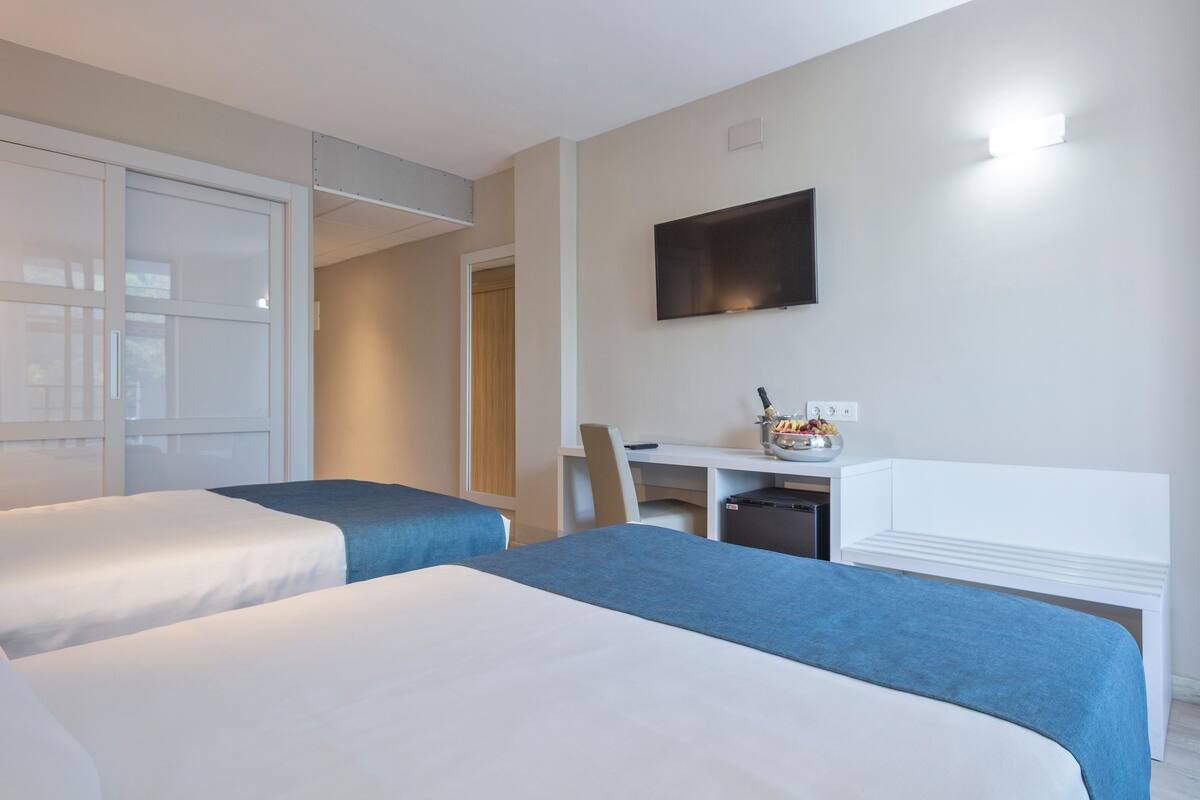 Een hotelkamer met twee bedden, een bureau, een stoel, een televisie en een kleine kitchenette.