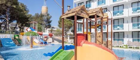 A water park area with slides and a pool, surrounded by a building with balconies.