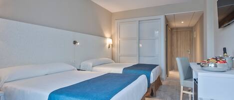 A hotel room with two beds, a desk with a fruit bowl, and a chair.