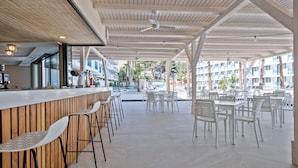 Un espace extérieur moderne, aménagé avec des chaises et des tables blanches, un comptoir de bar en bois et des ventilateurs de plafond.