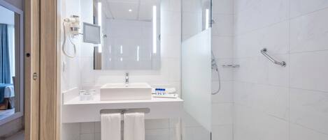 Un baño moderno con ducha acristalada, un lavabo blanco y un espejo encima.