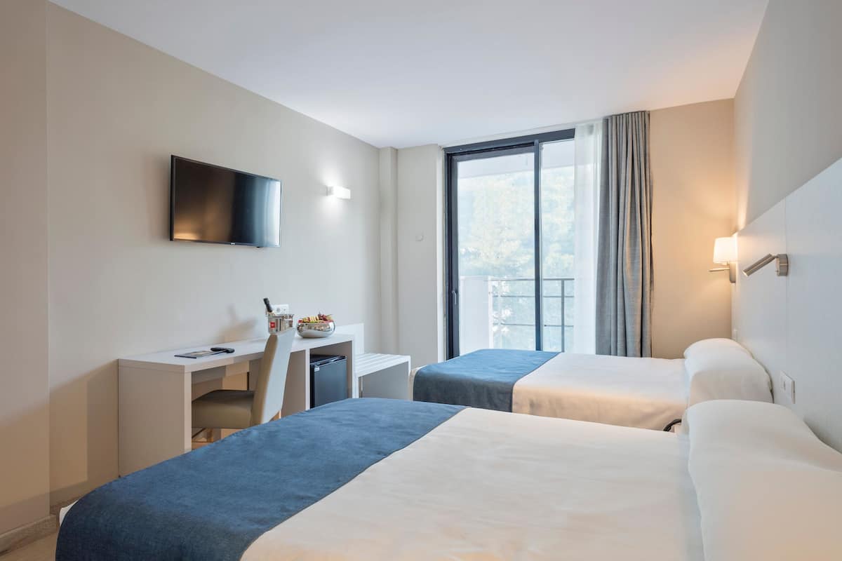 Een hotelkamer met twee bedden, een bureau, een televisie en een raam met gordijnen.