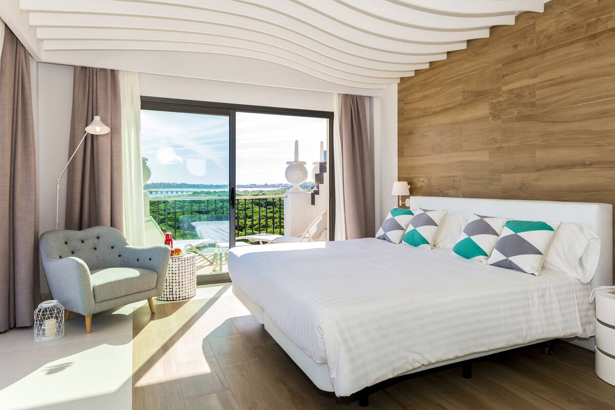 Habitación de hotel moderna con una cama grande, vistas a la vegetación y un revestimiento de pared de madera.