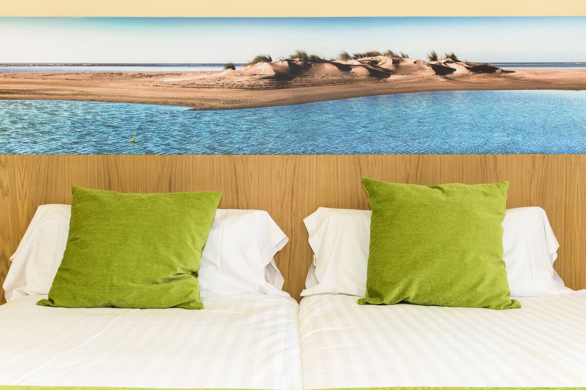 Una cama con sábanas blancas y dos almohadas verdes, frente a un cabecero de madera.