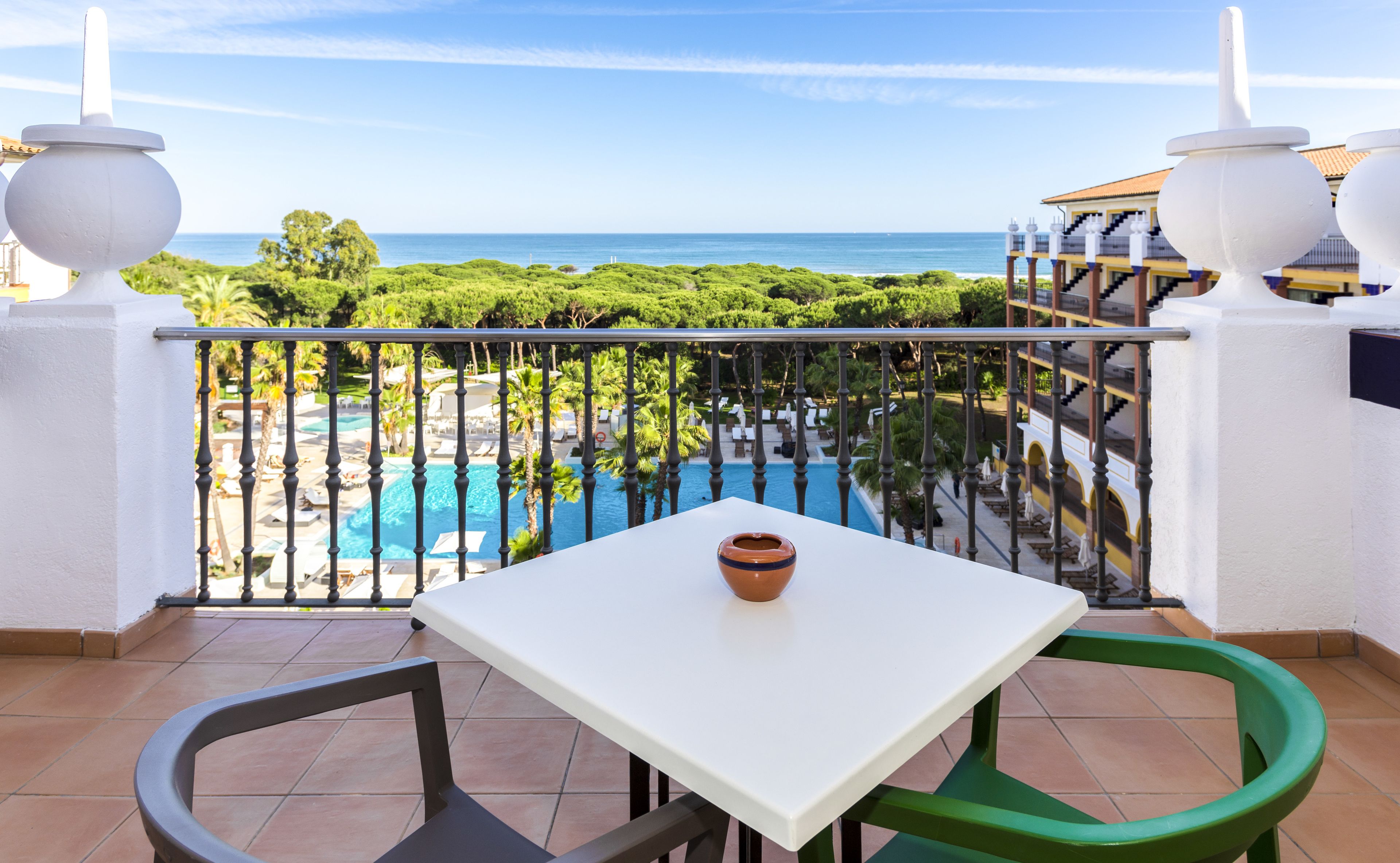 Ein Balkon mit weißem Tisch und Stühlen, der auf einen Pool und üppiges Grün blickt.