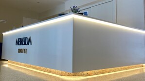 Un comptoir d’accueil d’hôtel au design moderne, agrémenté d’une plaque nominative portant l’inscription « HÔTEL NEREIDA ».