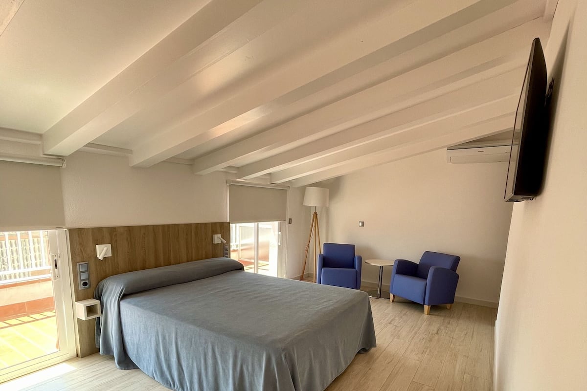 Een ruime slaapkamer met een groot bed, een bureau, twee stoelen en een televisie die aan de muur is bevestigd.