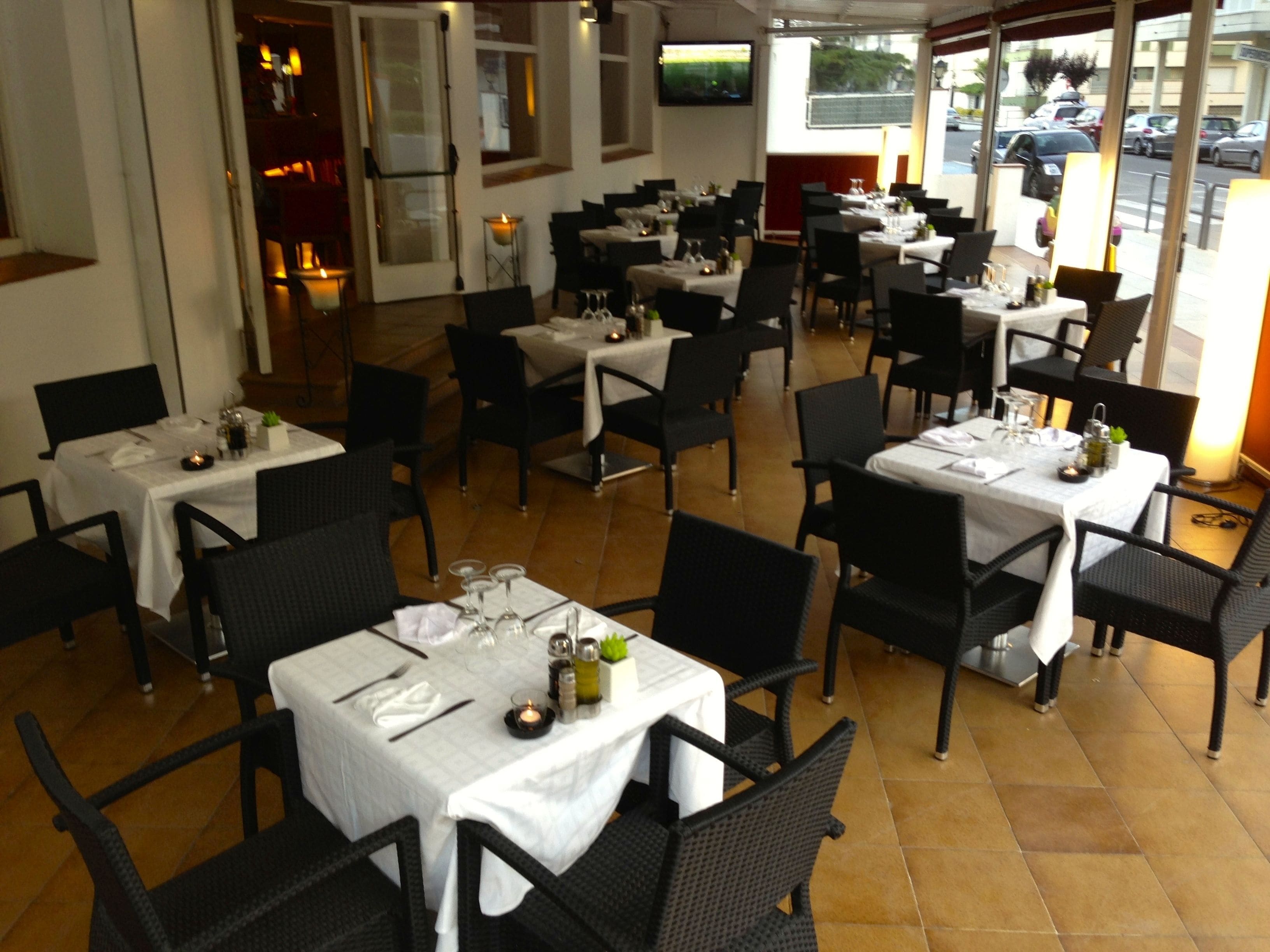 Un restaurante con varias mesas y sillas, cada conjunto con manteles blancos y velas.