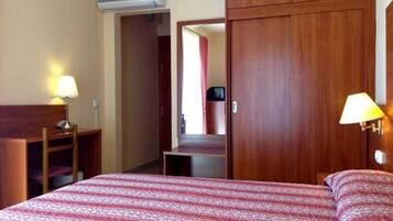 Una habitación de hotel con una cama, dos lámparas de noche, un armario de madera y un equipo de aire acondicionado.