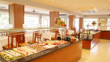 Uma área de buffet com diversas opções de comida, um espaço de refeições com mesas e cadeiras, e um arranjo decorativo.