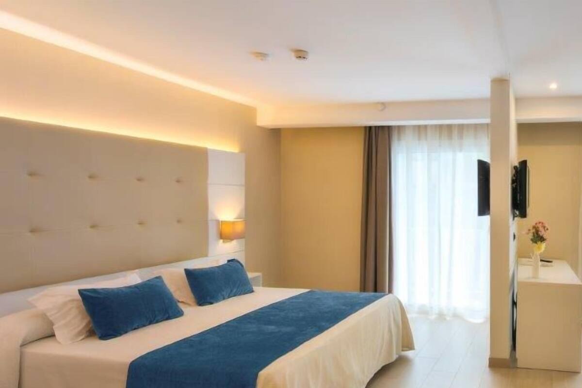 Habitación de hotel con una cama grande, una mesita de noche, un televisor de pantalla plana y una ventana con cortinas.