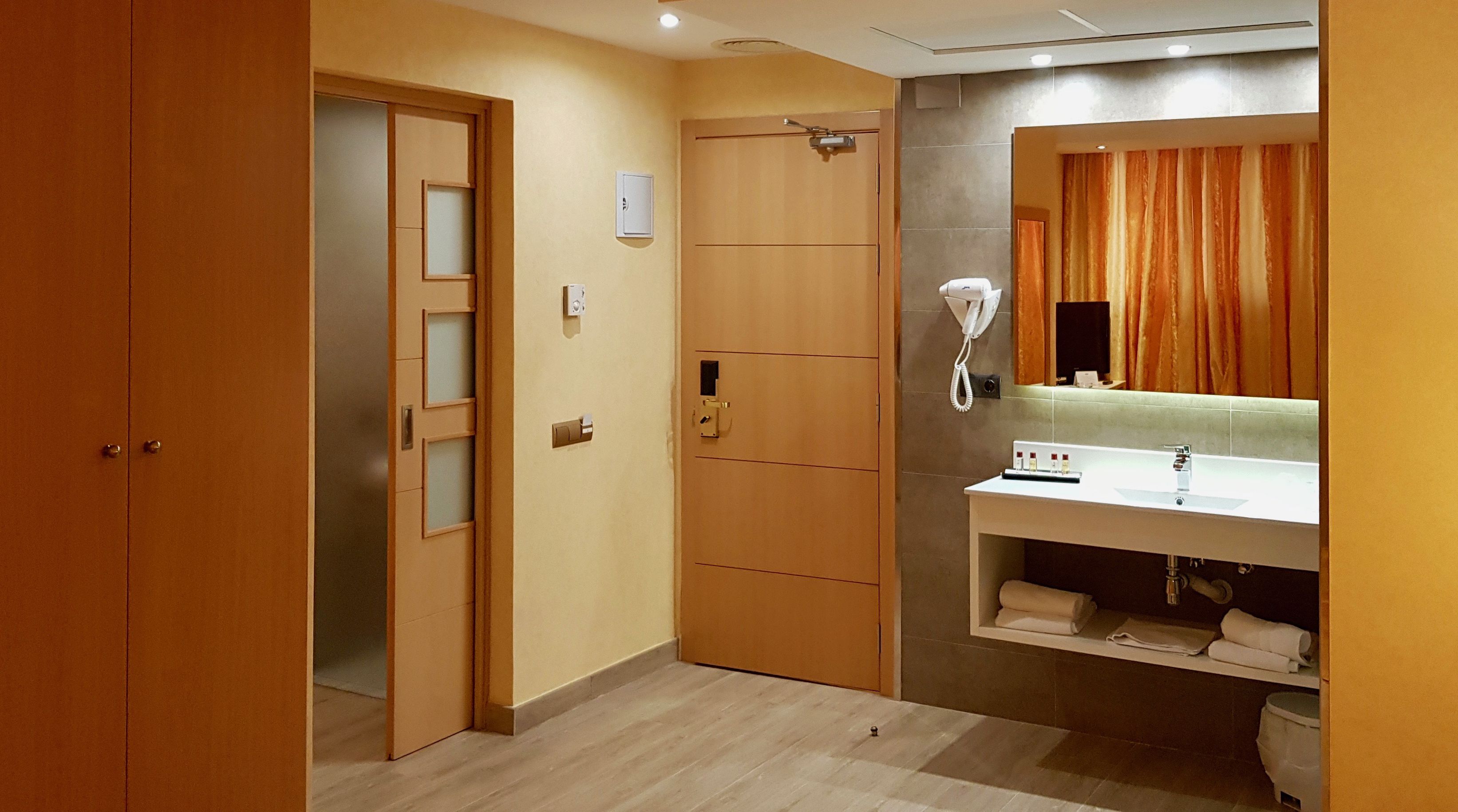 A hotel bathroom with a wooden door, a white sink with a mirror, and a towel rack.