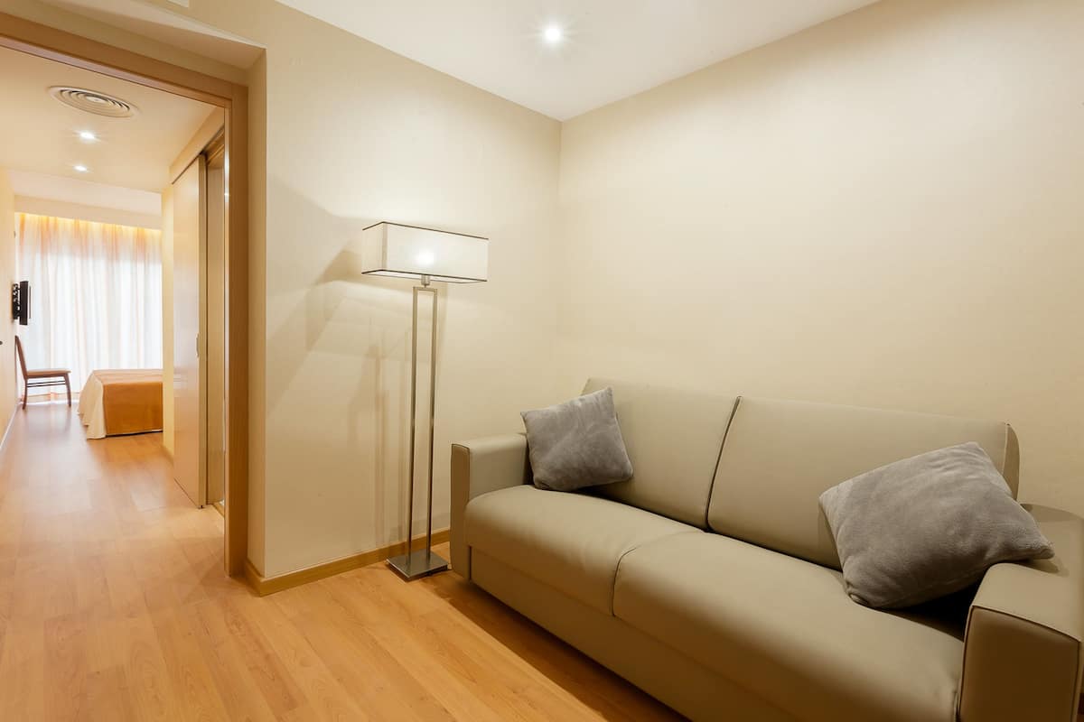 Un salón moderno con un sofá color beige, dos cojines grises, una lámpara de pie y suelo de madera.