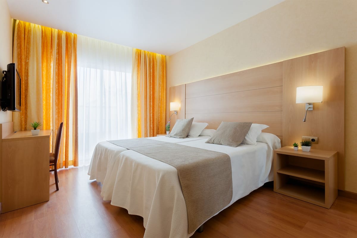 Una habitación de hotel con una cama grande, dos mesitas de noche con lámparas, un escritorio y una silla.